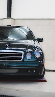 A sleek black Mercedes-Benz car positioned indoors under bright lighting, showcasing its glossy finish and classic front design with a prominent grille and pair of round headlights.