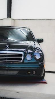 A beautifully polished classic Mercedes-Benz parked outside the garage under warm sunlight.