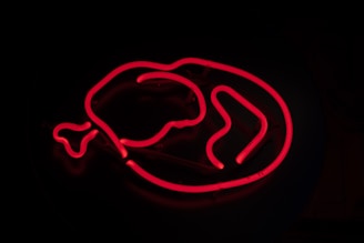 A glowing red neon sign in the shape of a chicken drumstick on a dark background.