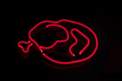 A glowing red neon sign in the shape of a chicken drumstick on a dark background.