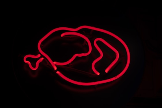 A glowing red neon sign in the shape of a chicken drumstick on a dark background.