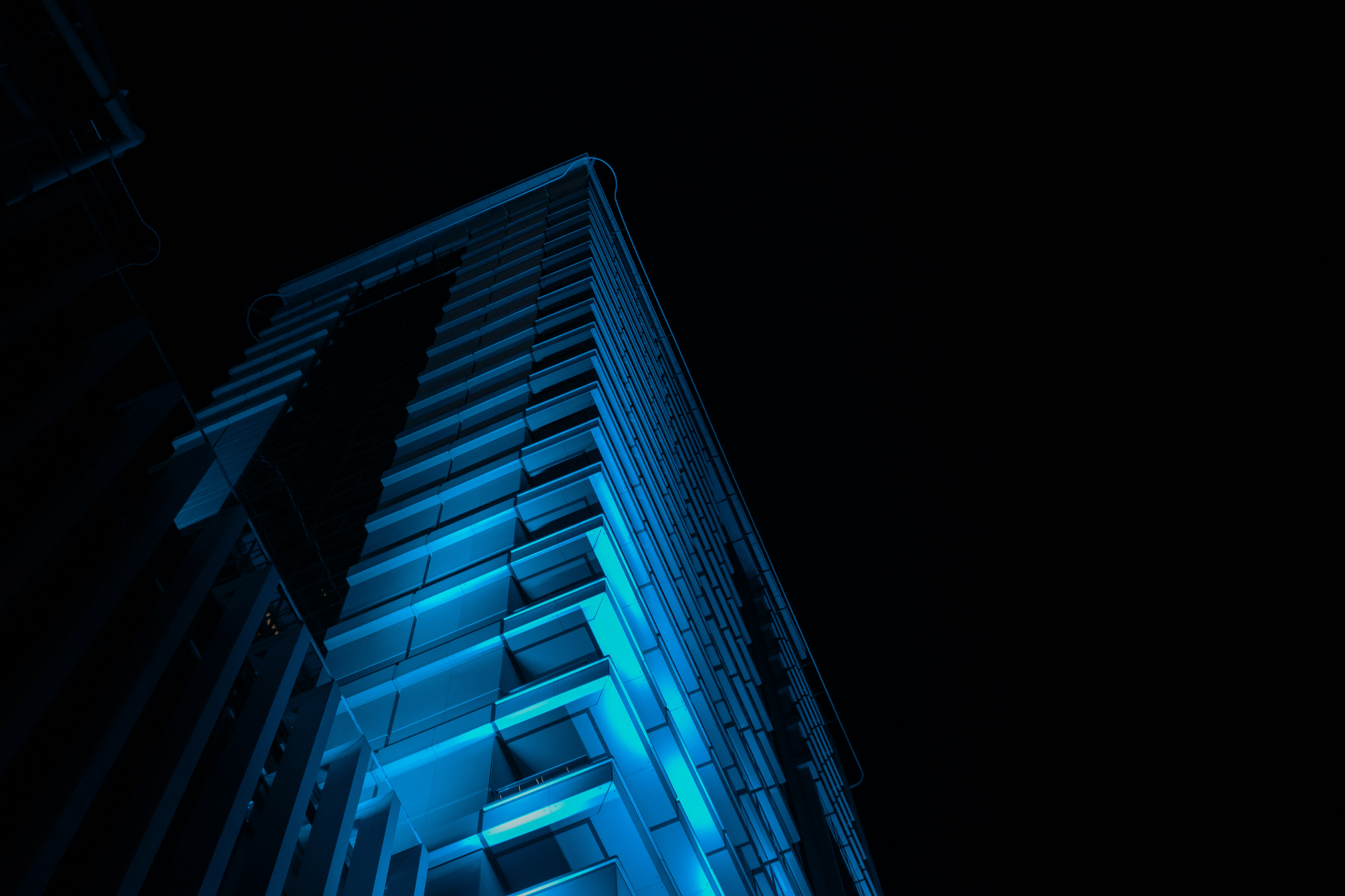 Modern residential building exterior with blue architectural lighting, clean facade, well-maintained entrance, and dark evening sky