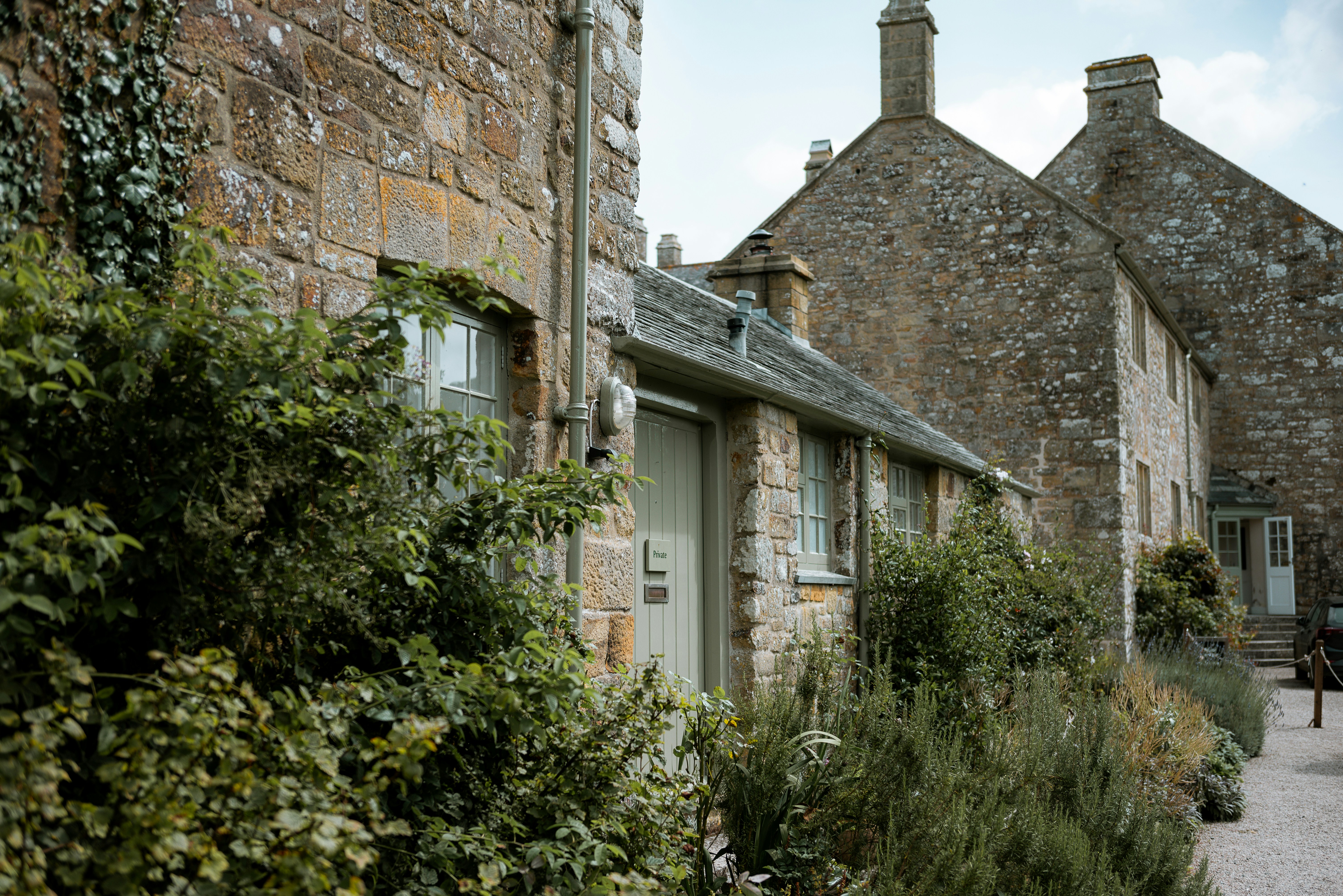 a stone building with a green door surrounded by greenery, 