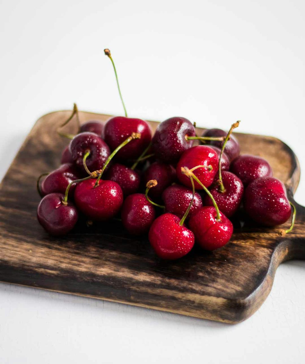 a wooden cutting board with a bunch of cherries on it