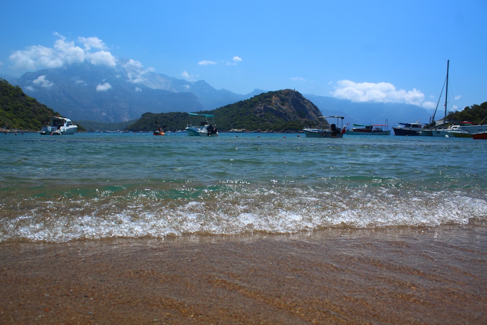 Una playa con barcos en el agua y montañas al fondo