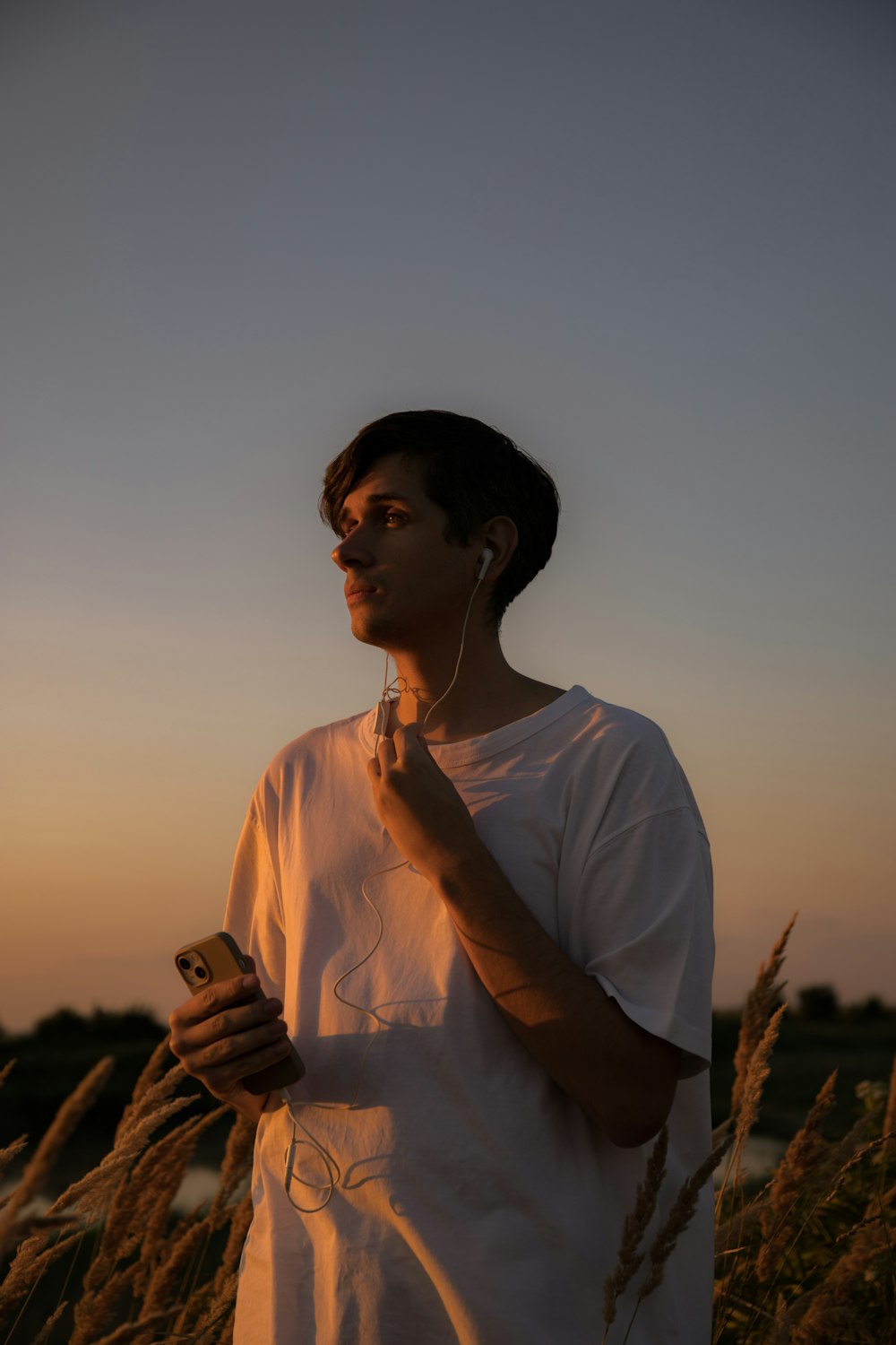 a man standing in a field of tall grass holding a cell phone