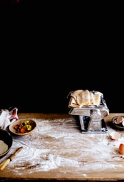 A rustic wooden table topped with a freshly baked pizza, scattered flour, and a rolling pin nearby.
