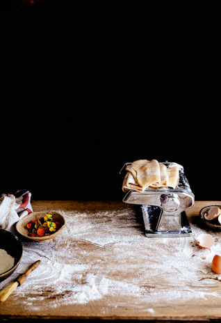Close-up of flour dusted wooden table with pasta-making tools scattered around.