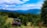 An off-road vehicle is parked in a lush, green landscape with dense forests and distant blue mountains under a partly cloudy sky. The vivid greenery and open field create a sense of adventure and tranquility.