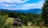 An off-road vehicle is parked in a lush, green landscape with dense forests and distant blue mountains under a partly cloudy sky. The vivid greenery and open field create a sense of adventure and tranquility.