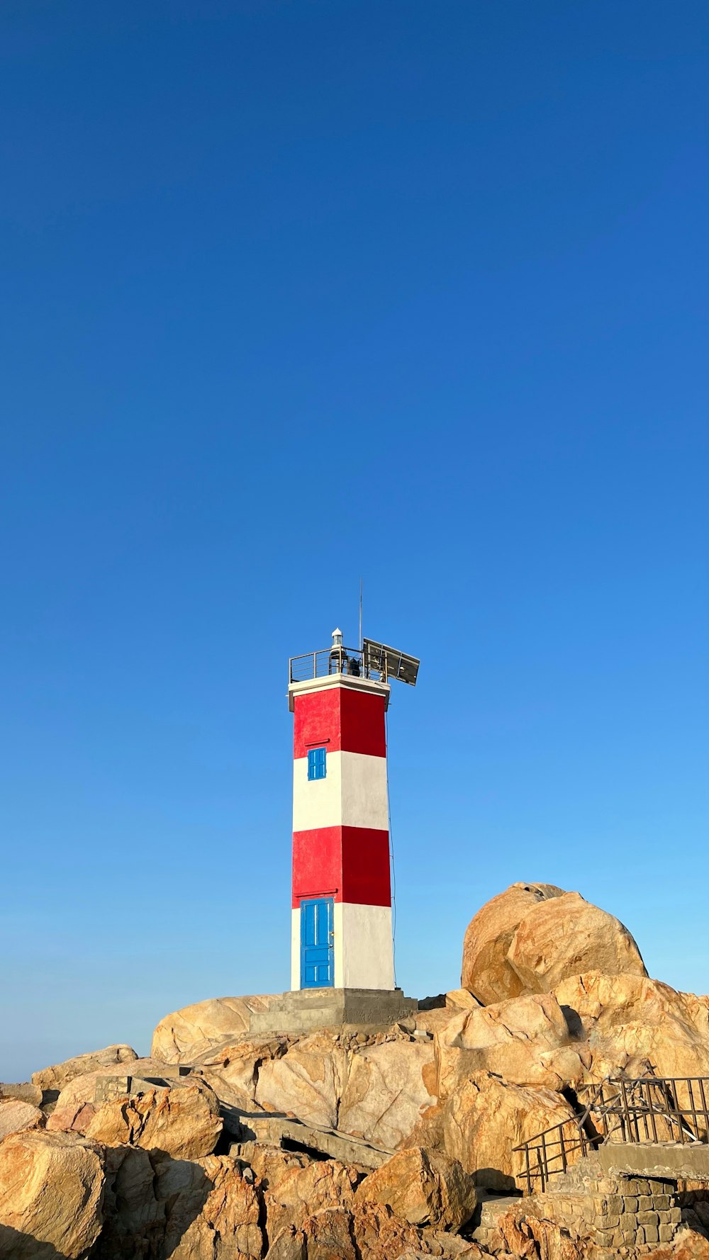 a red, white and blue lighthouse on a rocky shore