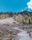 a truck driving down a dirt road next to a mountain
