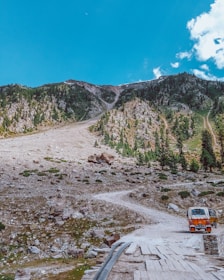 a truck driving down a dirt road next to a mountain