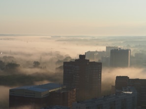A wide panoramic shot of a misty urban skyline at dawn, soft light bathing the buildings.