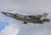 A modern military jet flies against a backdrop of cloudy sky. The aircraft is sleek with a gray camouflaged design, showcasing aerodynamic features and weapon mounts.