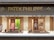 A luxury watch store display with the brand name Patek Philippe prominently featured at the top in gold letters. The window showcases an array of elegant watches on stands, surrounded by a soft, warmly lit interior. The backdrop includes artistic panels in shades of green and red, enhancing the refined appearance.