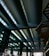 A modern architectural structure featuring a series of large, curved steel beams with skylight windows above. The space is expansive, with geometric lines and reflections of light on the glass surfaces of the walls.