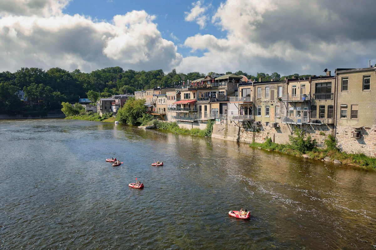 Old stone and brick buildings along the Grand River in Paris, Ontario, with rafters on the water