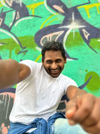 A cheerful model wearing a colorful t-shirt, smiling against a pastel-colored wall.