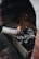 A tray filled with charcoal is being ignited with a fire starter, producing small flames and orange sparks. The setup appears to be in a grill or hearth environment, with bricks surrounding the area.