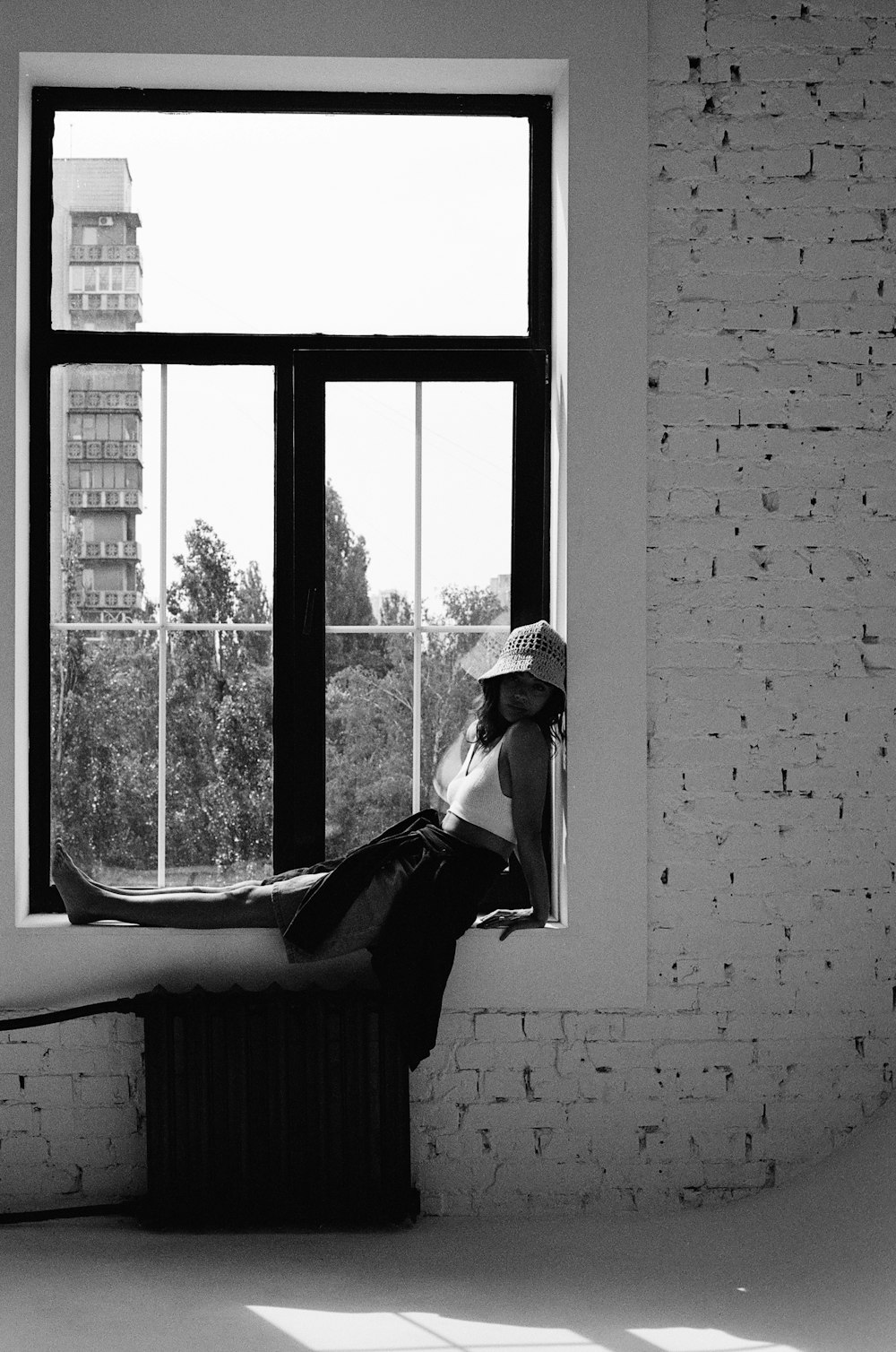 a black and white photo of a woman sitting on a window sill