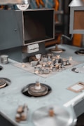 A vintage control panel with various knobs, switches, and dials. The machinery features metallic surfaces with a worn and industrial appearance. Some components look like they may be part of an old audio or film equipment setup.