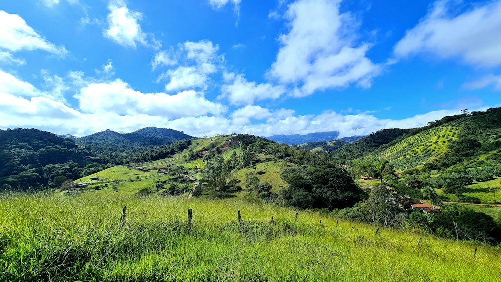 a lush green hillside surrounded by mountains under a blue sky