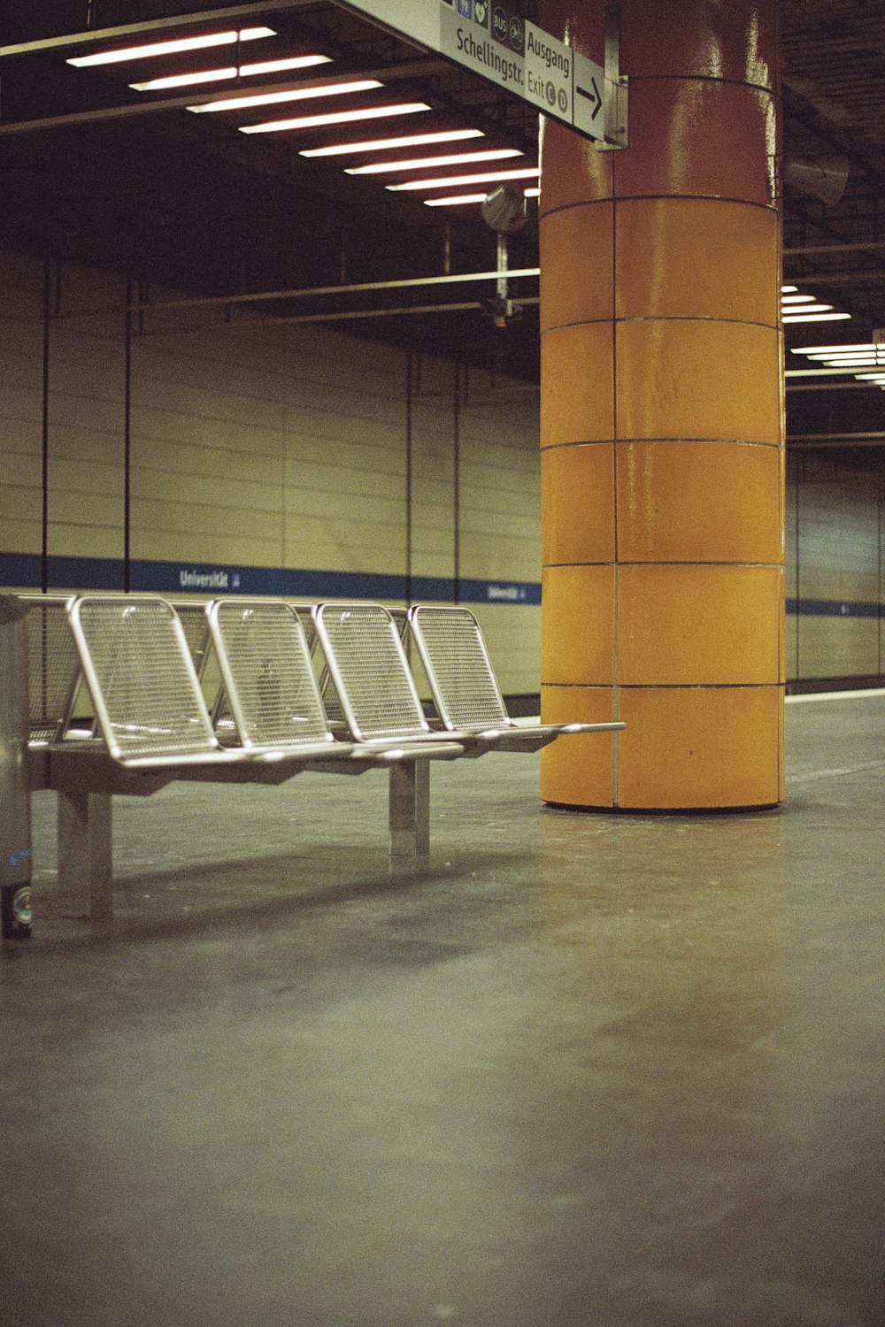 a row of metal benches sitting next to a yellow pillar