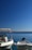 Two motorboats are moored in calm, clear blue water under a clear sky. The boat on the left has a Croatian flag attached to the side, and both boats have visible registration numbers. The horizon is visible in the distance.