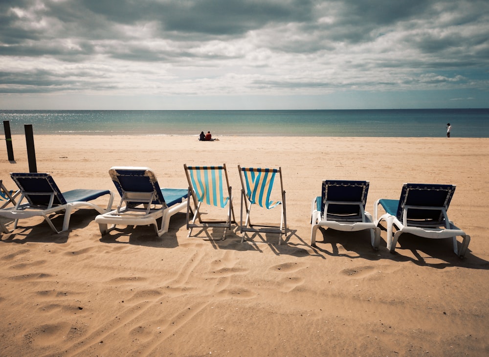 a row of lawn chairs sitting on top of a sandy beach
