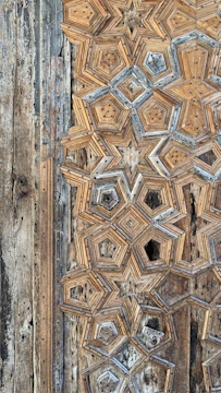 Close-up of master craftsmen carving intricate patterns into aged teak wood beams.