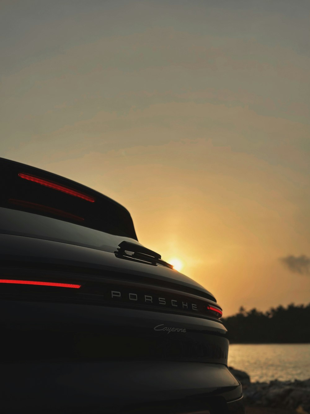 the back end of a black porsche parked in front of a body of water