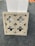A decorative stone panel featuring an intricate geometric pattern is positioned against a white rectangular structure. The panel displays symmetrical cut-out designs and is placed on a gray carpeted floor.