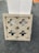 A decorative stone panel featuring an intricate geometric pattern is positioned against a white rectangular structure. The panel displays symmetrical cut-out designs and is placed on a gray carpeted floor.