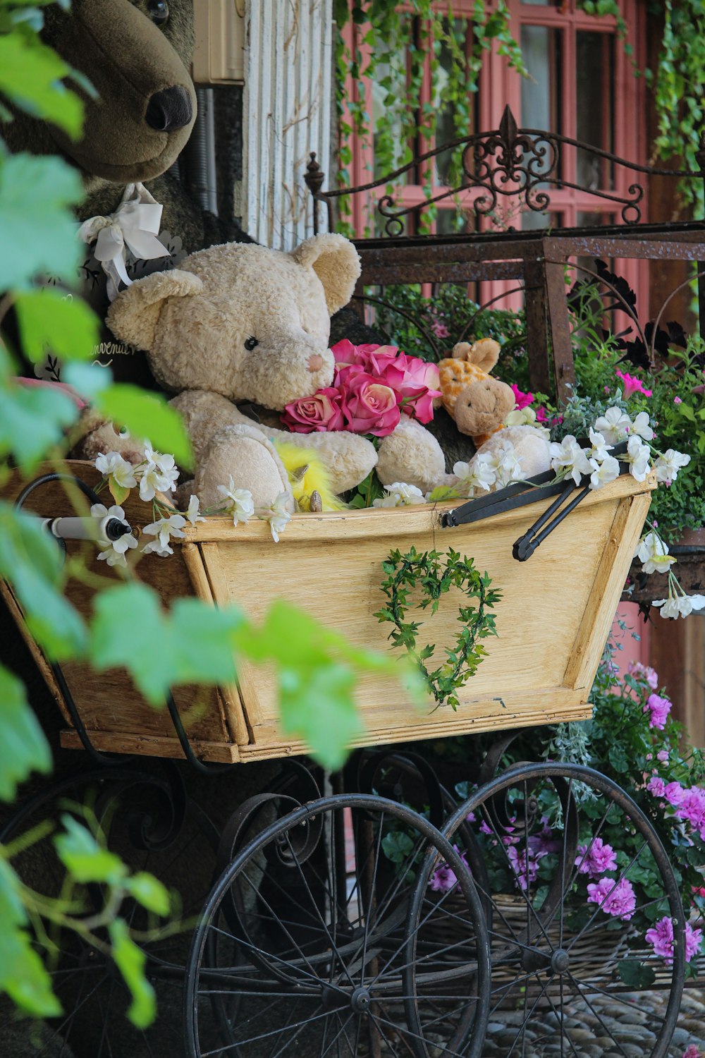 a teddy bear sitting on top of a wooden wagon filled with flowers