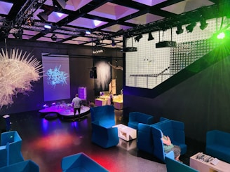 A vibrant interactive showroom featuring visitors engaging with mixed reality installations illuminated with teal and white lighting.