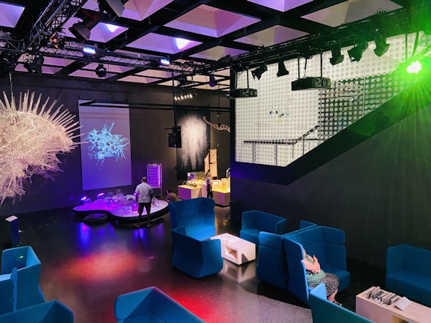 A vibrant interactive showroom featuring visitors engaging with mixed reality installations illuminated with teal and white lighting.