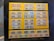 A collection of various banknotes is displayed behind glass on a bright yellow background. The banknotes are arranged in rows and columns and feature different colors, designs, and portraits. The display is mounted on a wall and surrounded by a dark frame.