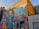 A vibrant mural on the side of a building with geometric patterns and shapes in various bright colors, featuring the text 'CREATIVITY IS IN ALL OF US'. The mural is located at the London Graphic Centre. The background includes a yellow brick wall and other urban elements such as doors and a lamp.