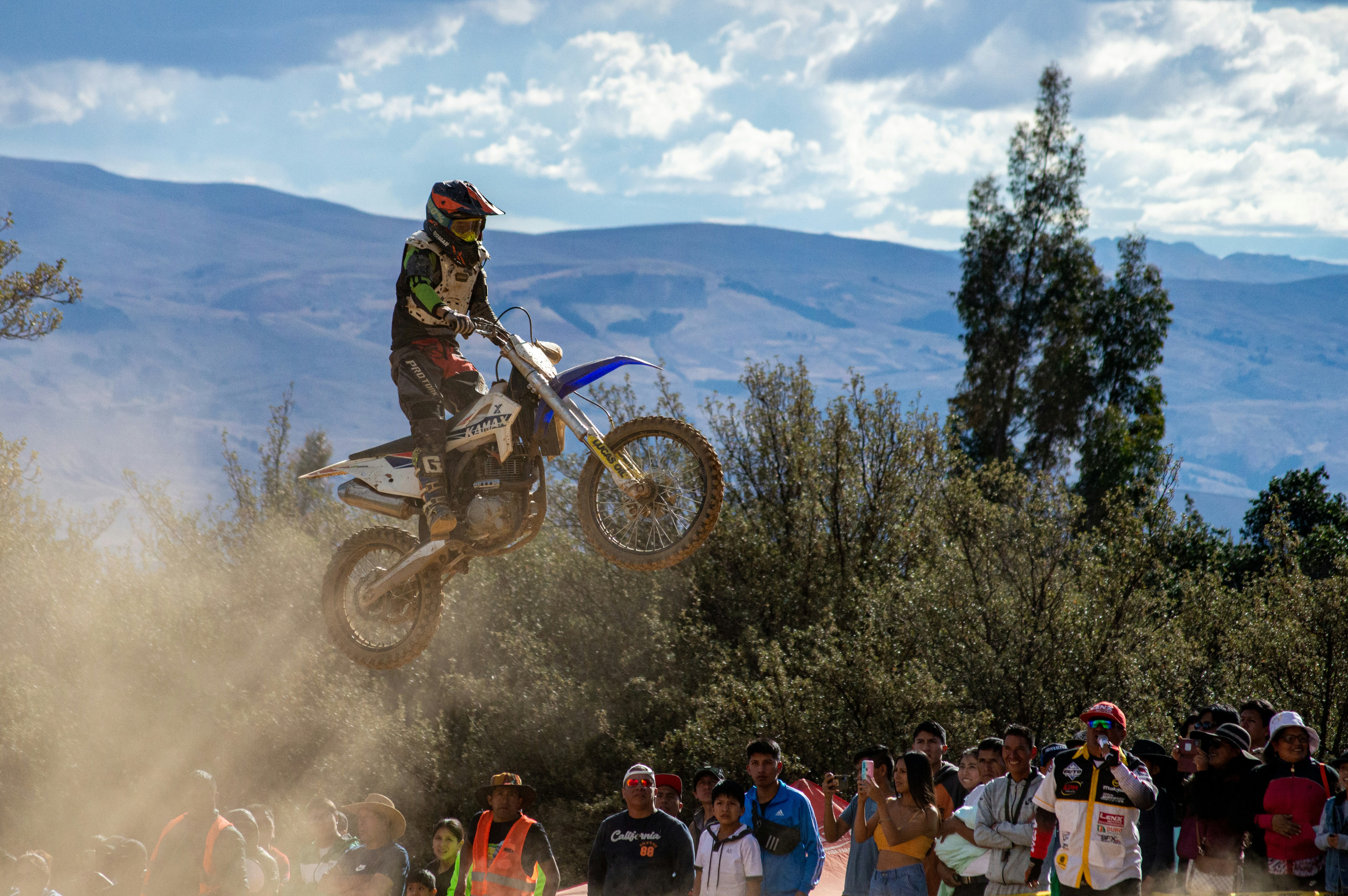 Close-up of a motocross rider wearing vyzus goggles, dust flying around under a sunset sky.