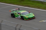 A sleek, bright green racing car with a large rear spoiler speeds along a track. The car features a number 33 and various sponsor logos are visible on its body. The aerodynamic design and vibrant color scheme suggest a high-performance vehicle.