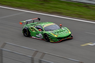 A sleek, bright green racing car with a large rear spoiler speeds along a track. The car features a number 33 and various sponsor logos are visible on its body. The aerodynamic design and vibrant color scheme suggest a high-performance vehicle.