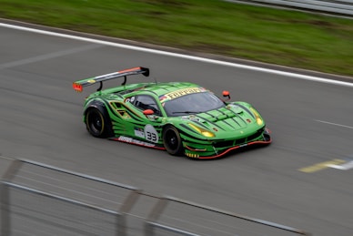 A sleek, bright green racing car with a large rear spoiler speeds along a track. The car features a number 33 and various sponsor logos are visible on its body. The aerodynamic design and vibrant color scheme suggest a high-performance vehicle.