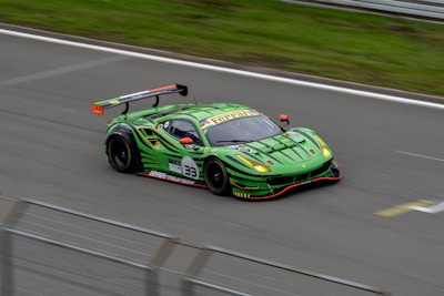 A sleek, bright green racing car with a large rear spoiler speeds along a track. The car features a number 33 and various sponsor logos are visible on its body. The aerodynamic design and vibrant color scheme suggest a high-performance vehicle.