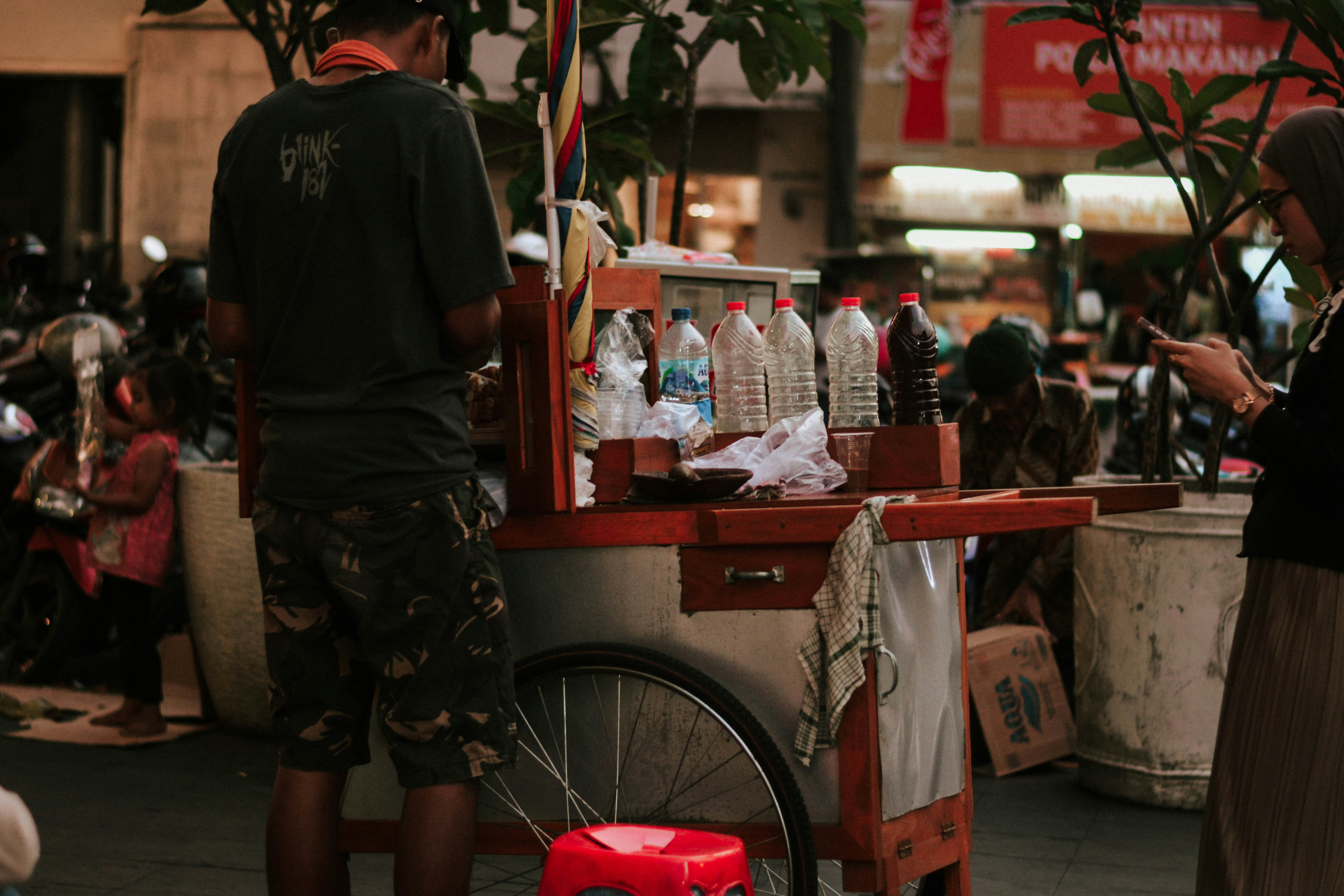 a man standing next to a red cart filled with bottles, 
