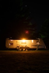 Night shot of a trailer illuminated with warm lights, showing its modular sections.