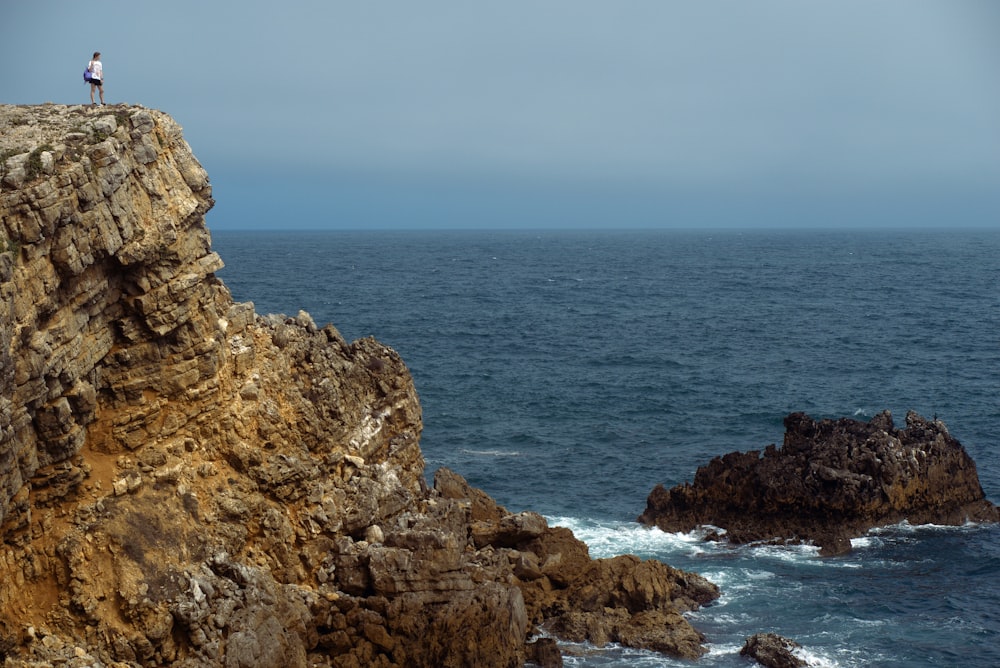 a person standing on top of a cliff next to the ocean