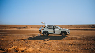 A driver opening the door of a luxury SUV beside a scenic desert road at sunset.
