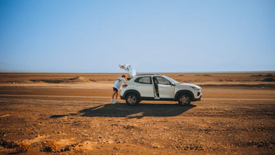 A driver opening the door of a luxury SUV beside a scenic desert road at sunset.