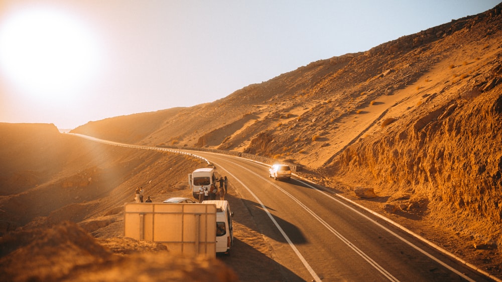 a couple of trucks driving down a road next to a hill